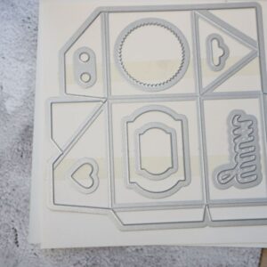 Baker’s Box Thinlits Dies arranged on storage sheet with box and decorative elements